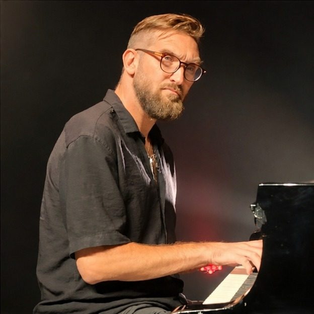 Tamir Hitman playing a grand piano under stage lighting